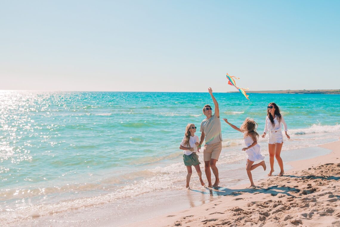 Familia feliz disfrutando la playa volando un papalote