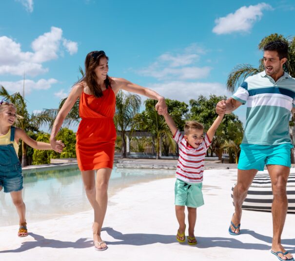 Feliz familia caminando y tomados de la mano junto a la piscina