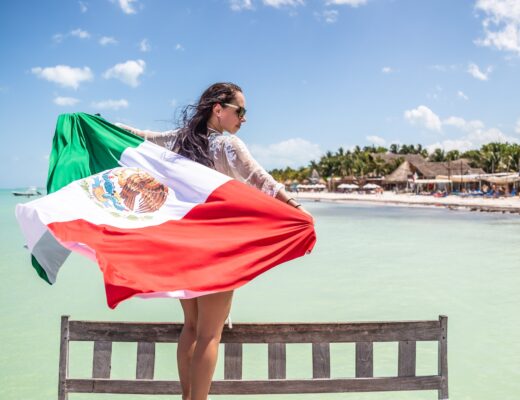 Mujer patriótica mexicana sostiene una bandera nacional de pie en un banco frente al mar en la playa