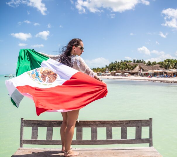 Mujer patriótica mexicana sostiene una bandera nacional de pie en un banco frente al mar en la playa