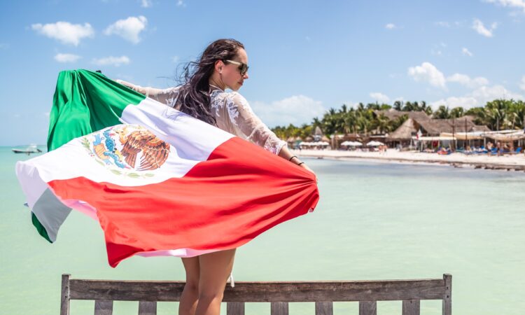 Mujer patriótica mexicana sostiene una bandera nacional de pie en un banco frente al mar en la playa